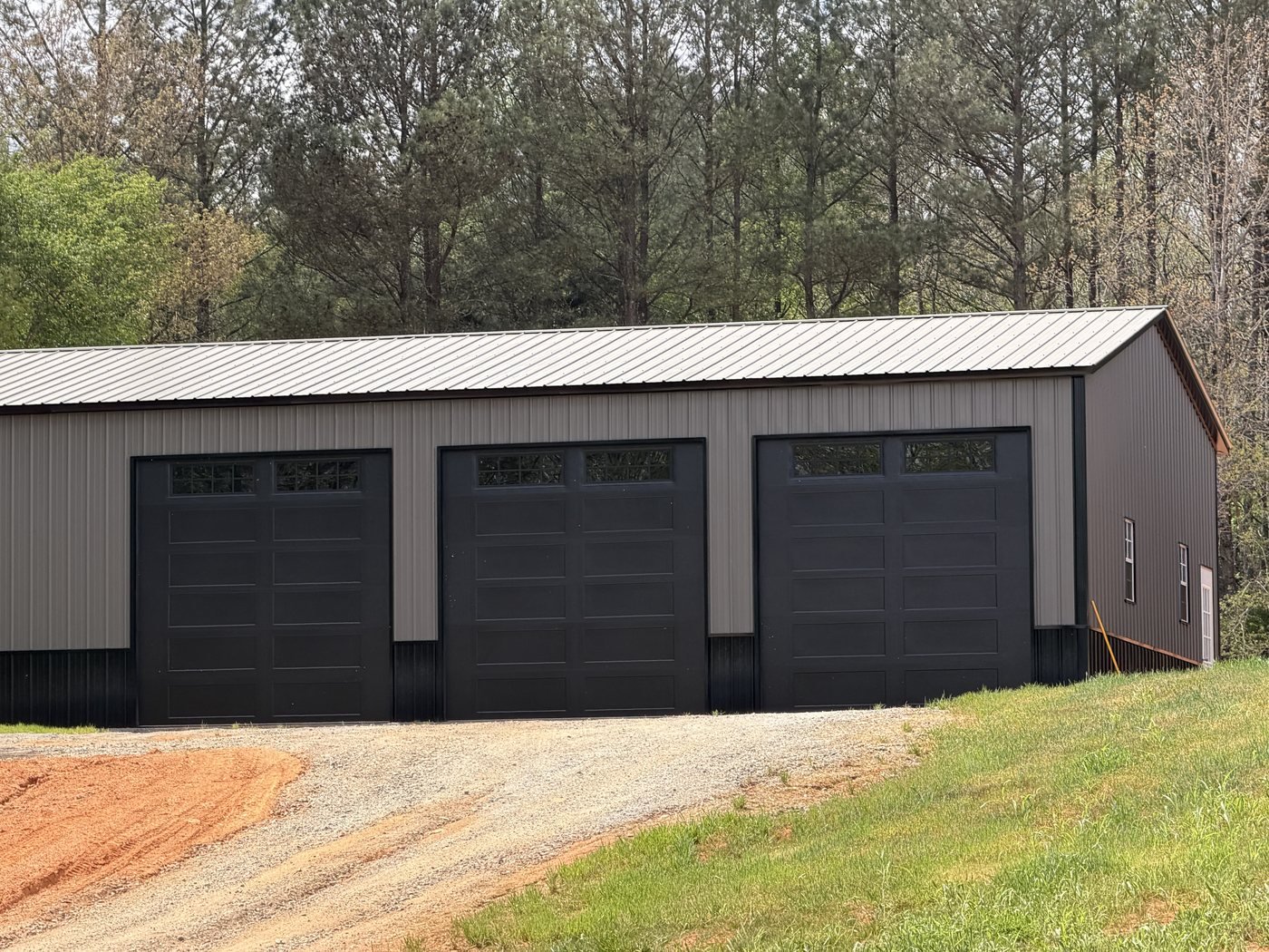 Three black carriage-panel garage doors on a tan steel building