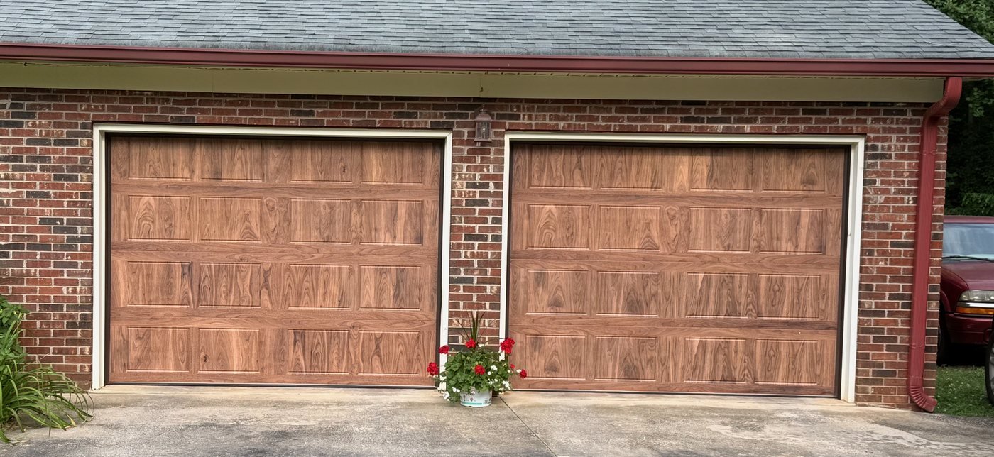 Two traditional woodgrain long-panel garage doors on a red brick home